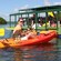 Two people sitting on a kayak at a wooden dock smile at the camera with paddles in their hands